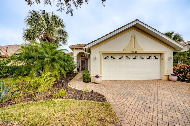 view of front facade featuring decorative driveway, an attached garage, a tile roof, and stucco siding