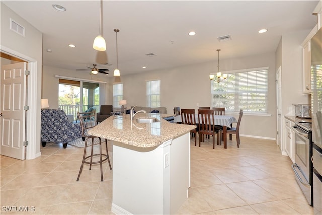 kitchen featuring a breakfast bar area, an island with sink, hanging light fixtures, and electric range