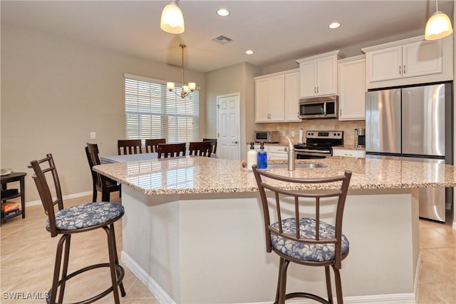 kitchen featuring stainless steel appliances, a kitchen island with sink, white cabinets, and a kitchen bar