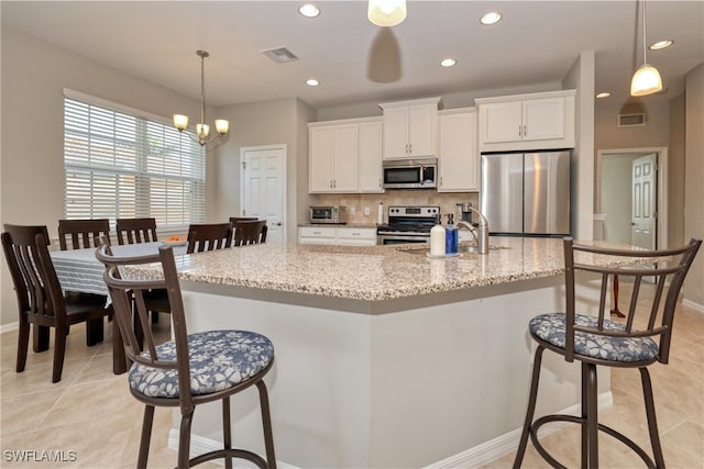 kitchen with light stone countertops, white cabinetry, appliances with stainless steel finishes, and an island with sink