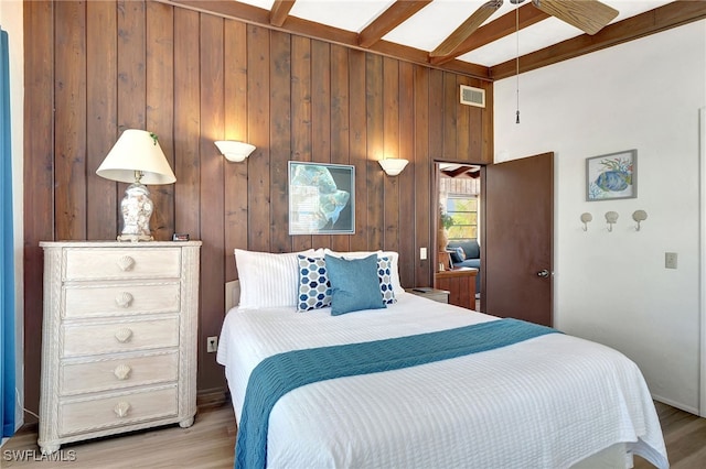 bedroom featuring wooden walls, beam ceiling, and light hardwood / wood-style flooring