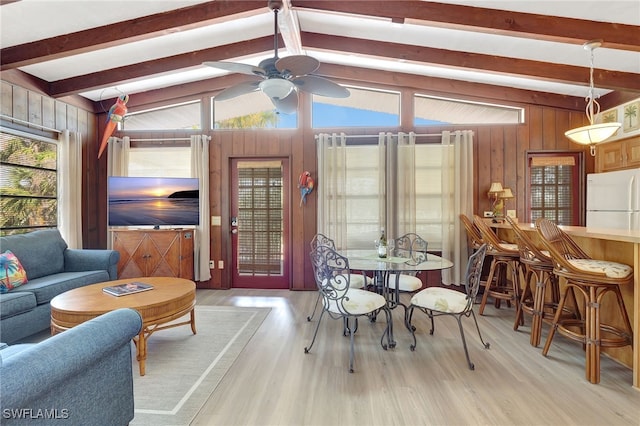 dining area with vaulted ceiling with beams, wooden walls, and light wood-type flooring