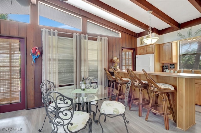 dining room featuring vaulted ceiling with beams, wooden walls, a healthy amount of sunlight, and light wood-type flooring