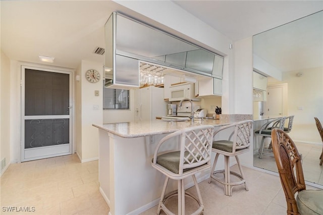 kitchen featuring white appliances, a kitchen breakfast bar, kitchen peninsula, and white cabinets