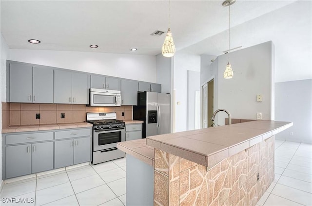 kitchen featuring tasteful backsplash, tile counters, lofted ceiling, appliances with stainless steel finishes, and hanging light fixtures