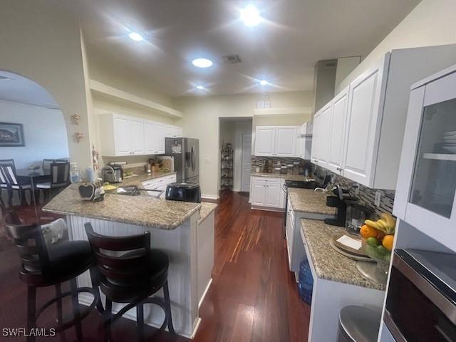 kitchen with a peninsula, white cabinetry, a kitchen breakfast bar, appliances with stainless steel finishes, and tasteful backsplash