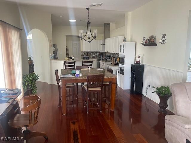 dining room featuring a chandelier, arched walkways, visible vents, and dark wood finished floors