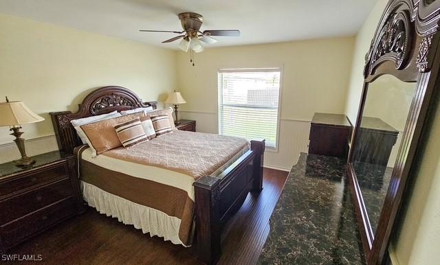 bedroom with dark wood finished floors, a ceiling fan, and wainscoting