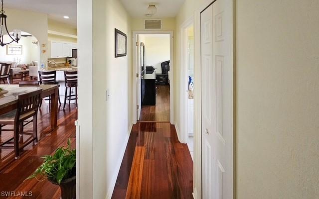 hallway featuring baseboards, visible vents, dark wood finished floors, a chandelier, and recessed lighting