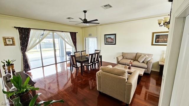 living area featuring ornamental molding, visible vents, dark wood-type flooring, and ceiling fan with notable chandelier