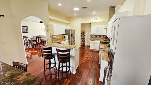 kitchen with arched walkways, a peninsula, visible vents, freestanding refrigerator, and stainless steel fridge with ice dispenser