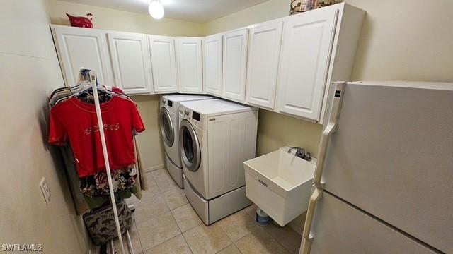 clothes washing area featuring light tile patterned floors, cabinet space, a sink, and separate washer and dryer