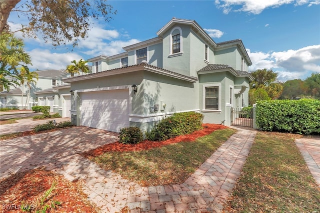 mediterranean / spanish-style house with a tile roof, stucco siding, decorative driveway, an attached garage, and a gate