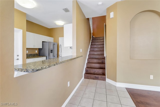 kitchen with white cabinetry, light stone countertops, high end refrigerator, and kitchen peninsula