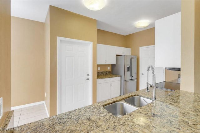 kitchen with light stone counters, light tile patterned floors, stainless steel refrigerator with ice dispenser, white cabinetry, and a sink