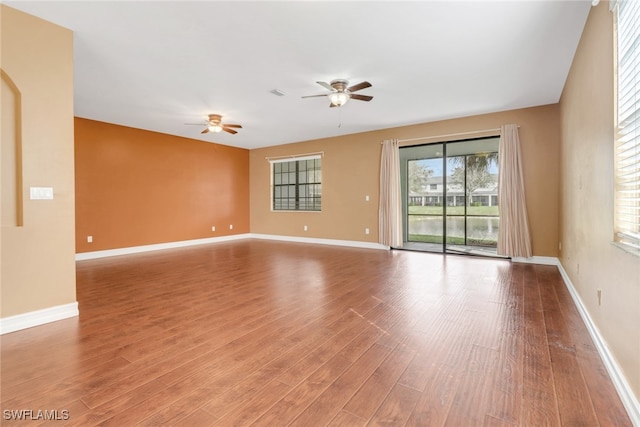 empty room featuring a ceiling fan, visible vents, wood finished floors, and baseboards