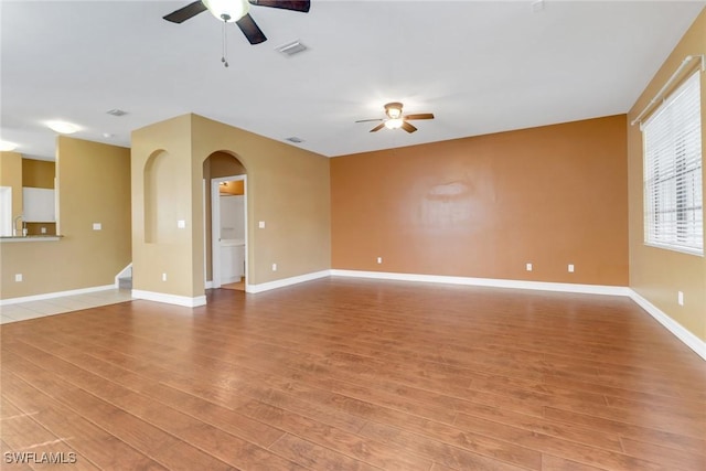 empty room with light wood-type flooring, arched walkways, visible vents, and ceiling fan