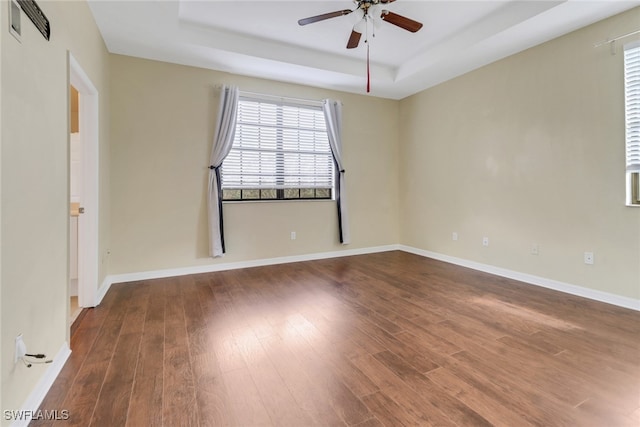 spare room with a tray ceiling, wood finished floors, and a ceiling fan