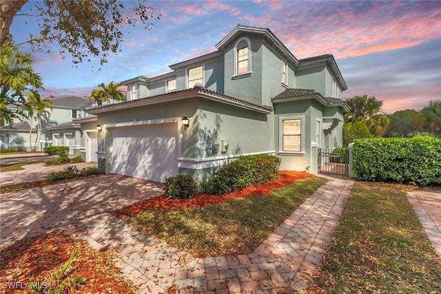view of front of home with a tile roof, stucco siding, decorative driveway, a garage, and a gate