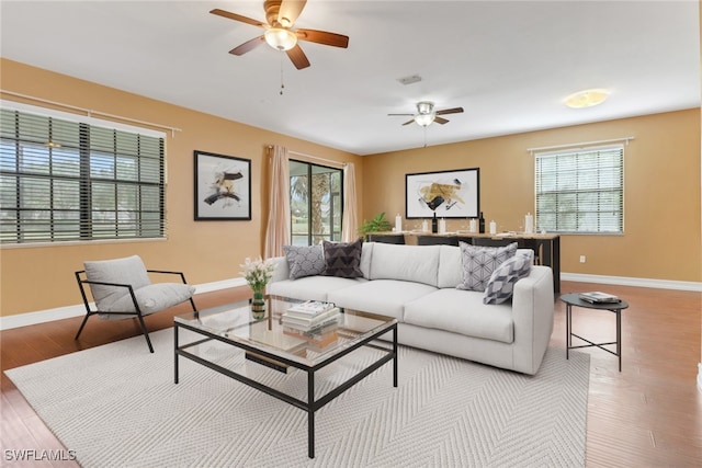 living room featuring plenty of natural light, baseboards, ceiling fan, and wood finished floors