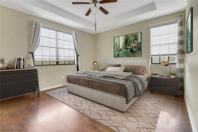 bedroom with ceiling fan, a tray ceiling, and light wood-type flooring