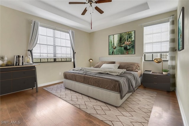 bedroom featuring light wood finished floors, ceiling fan, a raised ceiling, and baseboards