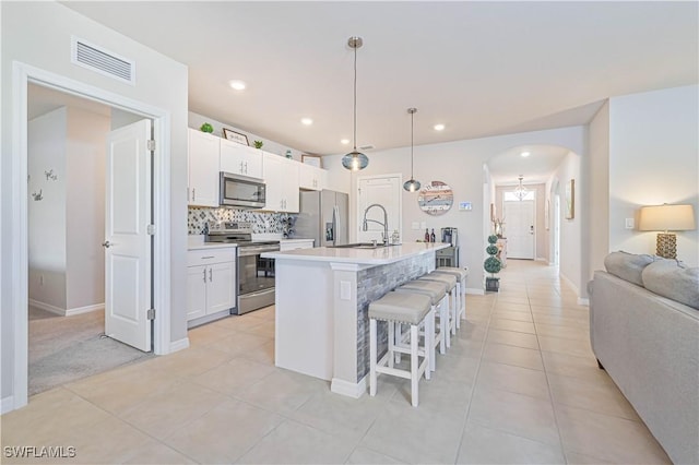 kitchen featuring a kitchen breakfast bar, pendant lighting, stainless steel appliances, a kitchen island with sink, and white cabinets