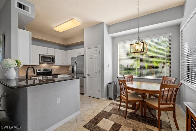 kitchen featuring light tile patterned flooring, kitchen peninsula, white cabinets, stainless steel appliances, and backsplash