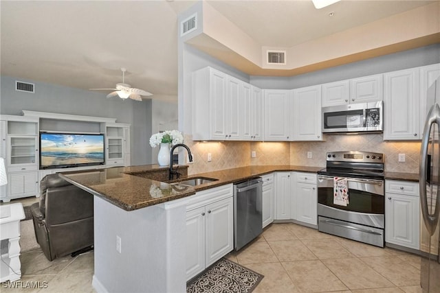 kitchen with appliances with stainless steel finishes, sink, white cabinets, dark stone counters, and kitchen peninsula