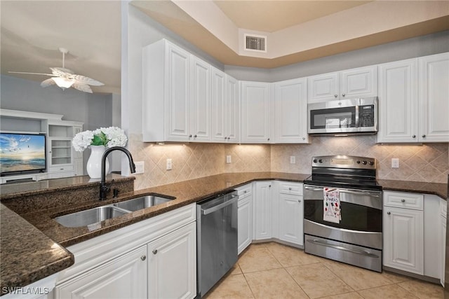 kitchen featuring sink, backsplash, stainless steel appliances, white cabinets, and dark stone counters