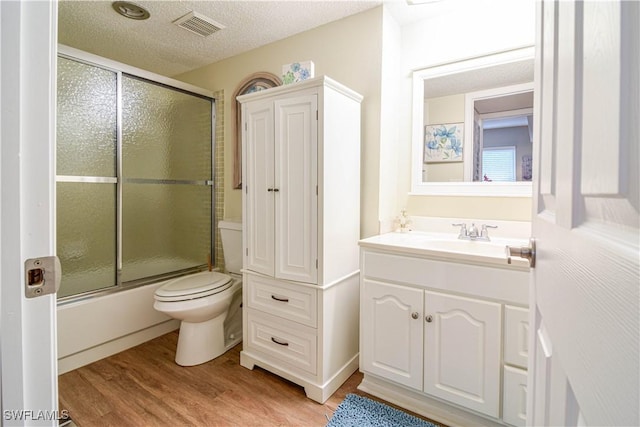 full bathroom featuring combined bath / shower with glass door, vanity, wood-type flooring, a textured ceiling, and toilet