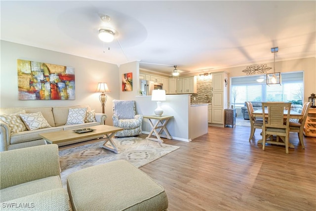 living room featuring ceiling fan, ornamental molding, and light wood-type flooring