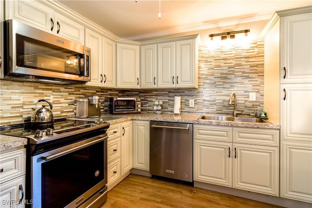 kitchen featuring sink, backsplash, stainless steel appliances, light stone countertops, and light wood-type flooring