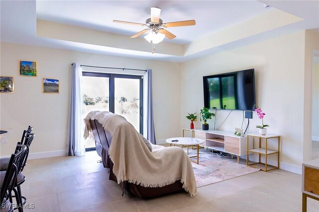 living room with a ceiling fan, a raised ceiling, and baseboards