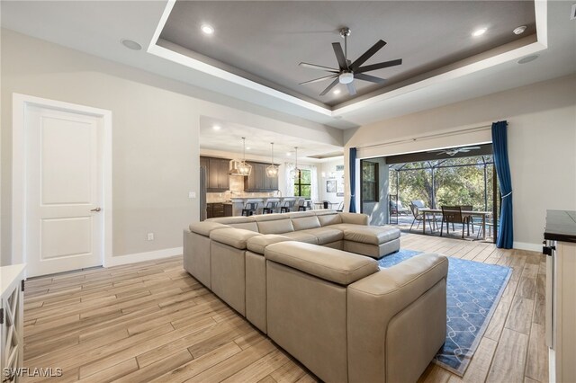 living room with ceiling fan, light hardwood / wood-style floors, and a tray ceiling