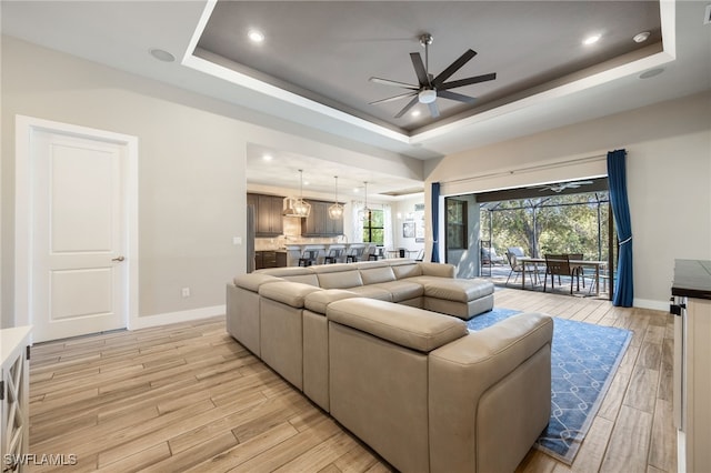 living room featuring ceiling fan, light hardwood / wood-style floors, and a tray ceiling