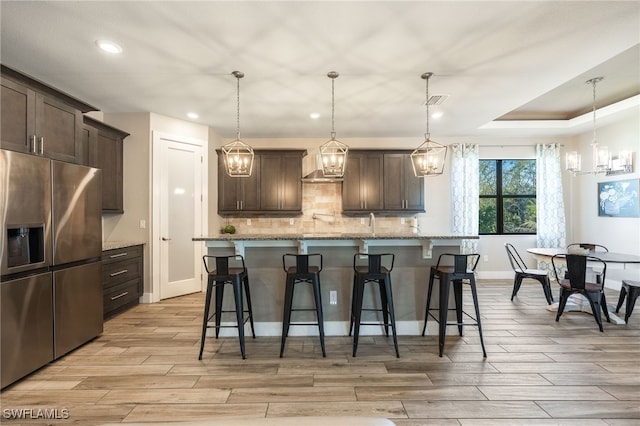 kitchen with stainless steel refrigerator with ice dispenser, an island with sink, dark brown cabinets, and pendant lighting