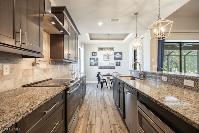 kitchen featuring wall chimney exhaust hood, sink, a raised ceiling, stainless steel appliances, and light stone countertops