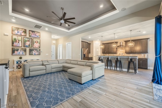 living room featuring ceiling fan, a tray ceiling, and light wood-type flooring