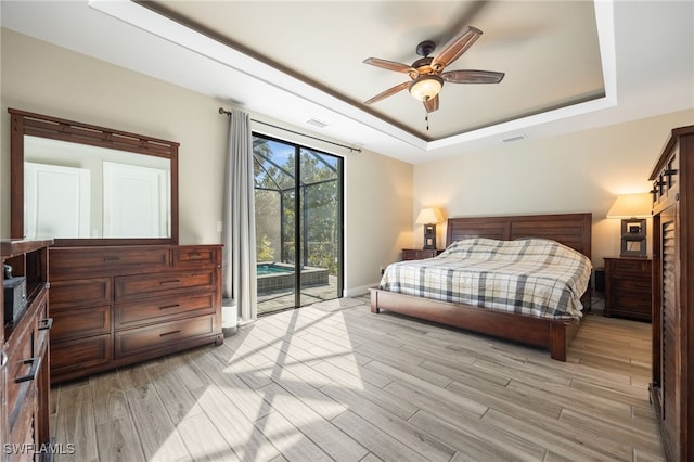 bedroom featuring access to exterior, light hardwood / wood-style floors, a raised ceiling, and ceiling fan