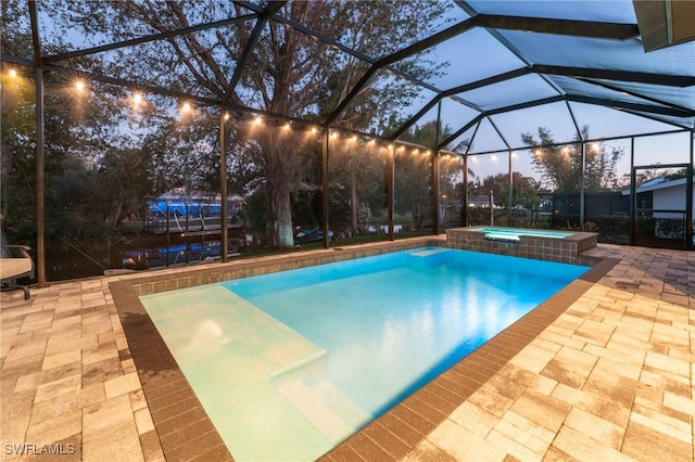 pool at dusk featuring an in ground hot tub, a patio area, and glass enclosure