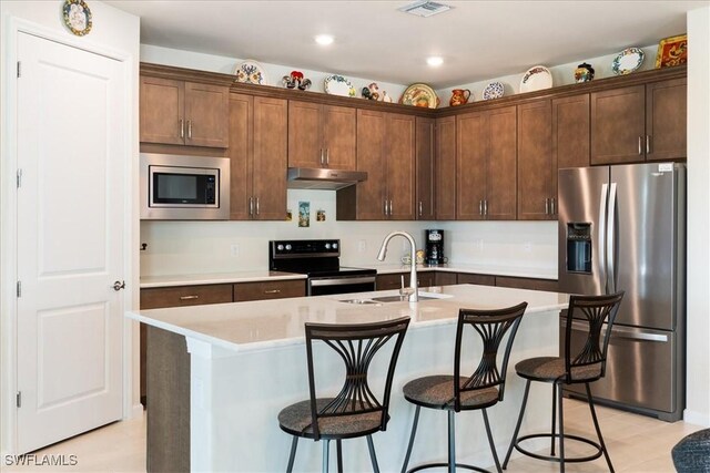 kitchen with sink, a center island with sink, a breakfast bar area, and appliances with stainless steel finishes