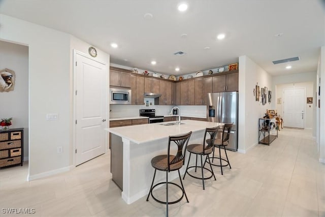 kitchen featuring stainless steel appliances, a breakfast bar area, sink, and a center island with sink