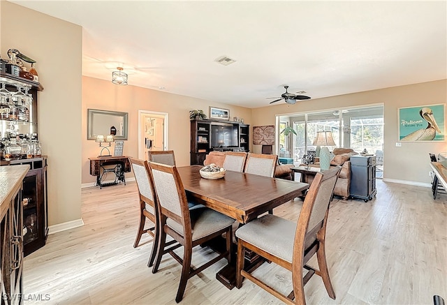 dining room with ceiling fan, bar area, and light wood-type flooring