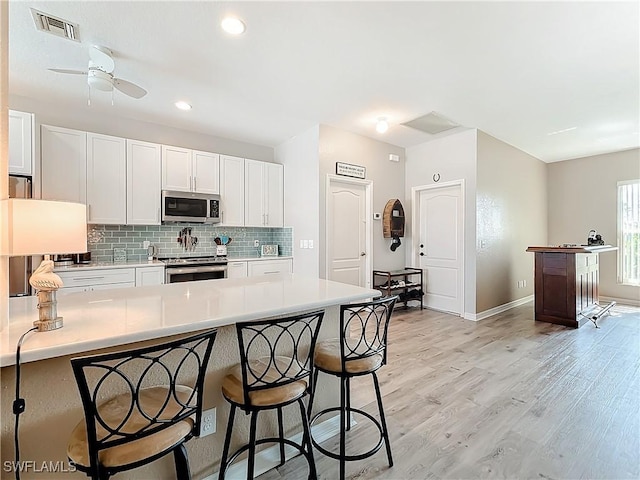 kitchen with appliances with stainless steel finishes, white cabinets, a kitchen bar, decorative backsplash, and light wood-type flooring