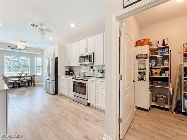 kitchen with tasteful backsplash, white cabinetry, ceiling fan, light hardwood / wood-style floors, and stainless steel appliances