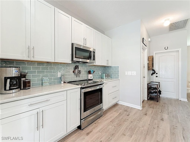 kitchen with white cabinetry, decorative backsplash, stainless steel appliances, and light wood-type flooring