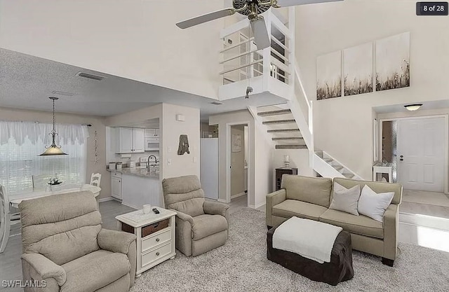 living area with a ceiling fan, a towering ceiling, visible vents, baseboards, and stairway