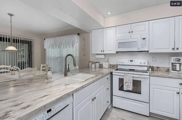 kitchen with decorative light fixtures, sink, white cabinets, light stone counters, and white appliances