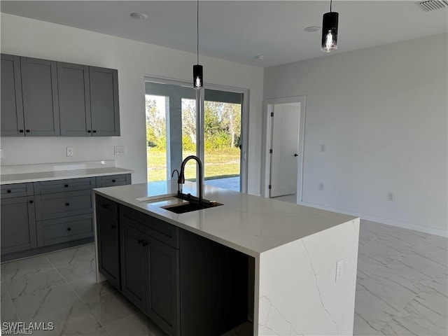 kitchen featuring pendant lighting, sink, gray cabinets, light stone counters, and a center island with sink